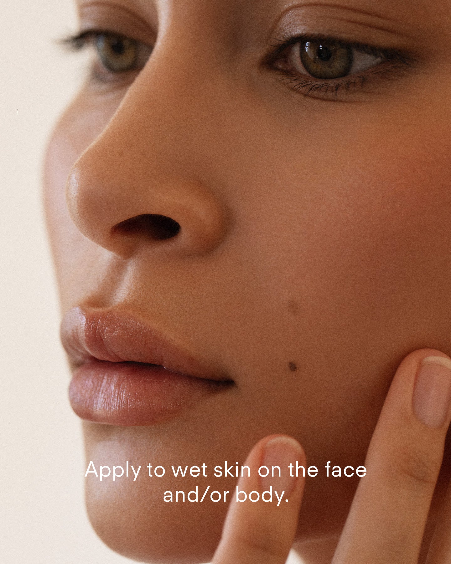A close-up of a person with clear, dewy skin gently touching their cheek. Text on image: Apply Ultra Gentle Exfoliating Gel with lactic acid to wet skin on your face and/or body.