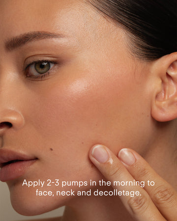 A close-up of a woman applying Ultra C Firming Concentrate to her cheek. The text reads: Use 2-3 pumps in the morning on face, neck, and decolletage to refine texture and brighten skin.