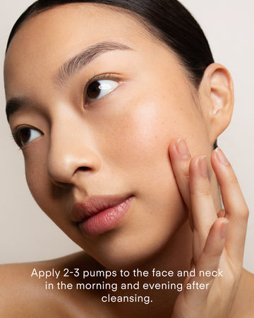 A woman gently applies Z Clear Shikimic Hydroxy-Biome Facial Serum to her cheek with her fingers. Text on the image reads, Apply 2-3 pumps in the morning to clean, dry skin.