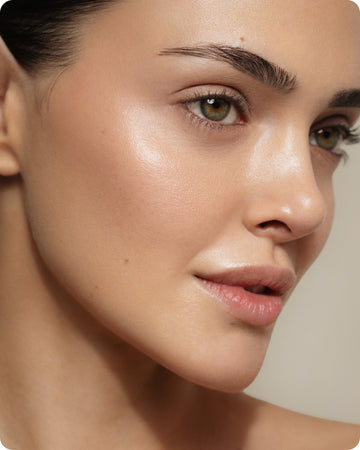 Close-up of a person's smooth, glowing skin, green eyes, groomed brows, and natural makeup—showing a clear complexion and soft lips—thanks to Ultra R.E.D Corrective Serum that helps reduce redness and soothe stressed skin.