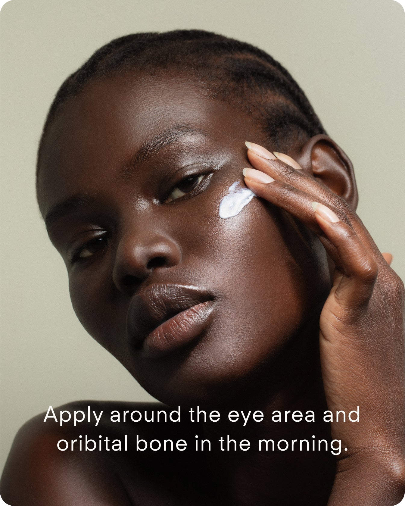 A person with dark skin applies Ultra C Firming Concentrate to their cheekbone with their fingers. Text: Apply around the eye area and orbital bone in the morning to brighten and refine skin texture.