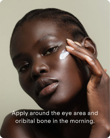 A person with dark skin applies Ultra C Firming Concentrate to their cheekbone with their fingers. Text: Apply around the eye area and orbital bone in the morning to brighten and refine skin texture.