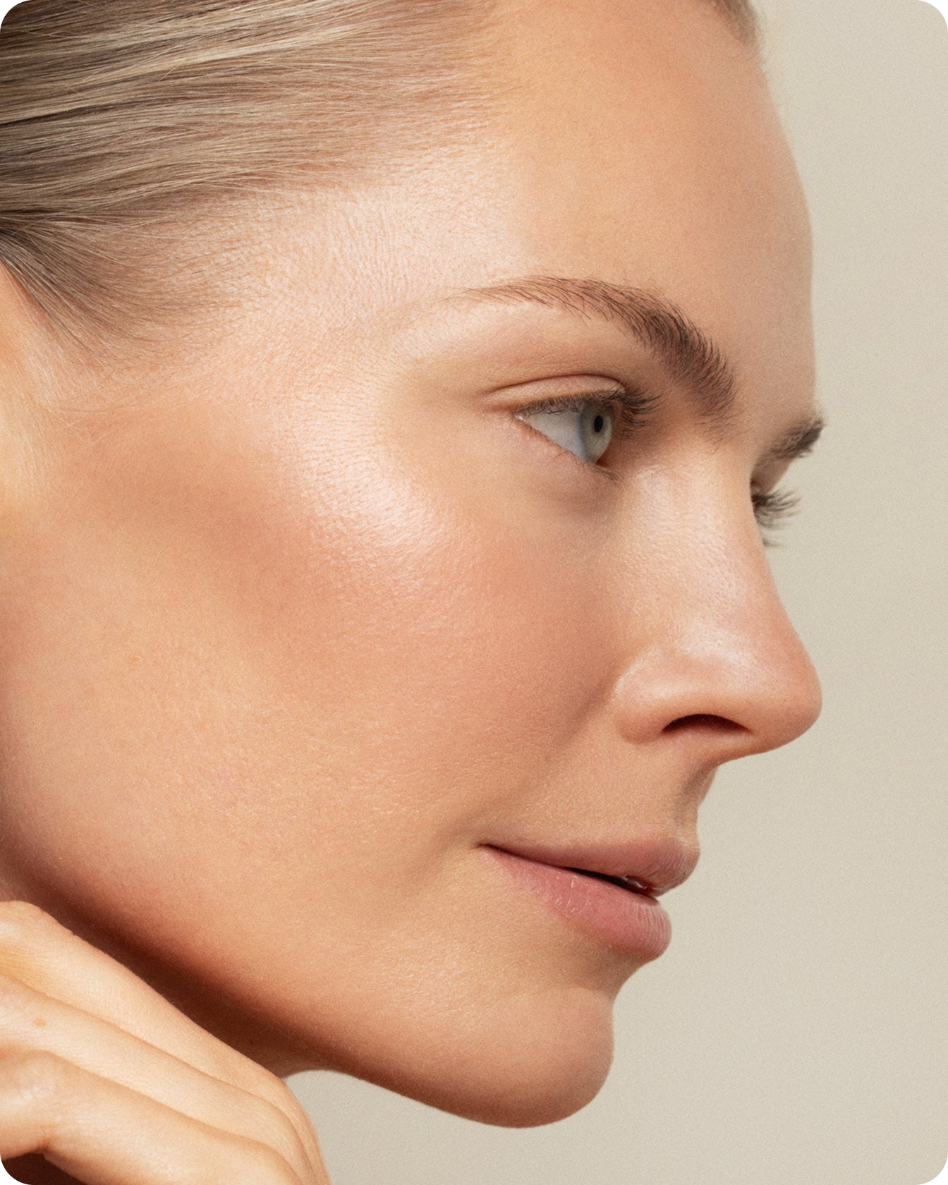Close-up side profile of a woman with smooth, clear skin and natural makeup, gently touching her chin. The neutral, soft background highlights the gentle overnight recovery effects of Ultra DNA³ Complex Recovery Night Cream.