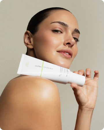 A woman with smooth, glowing skin confidently holds a white tube of Ultra UV Protective Daily Moisturiser SPF 30 Mattifying near her shoulder against a neutral background.