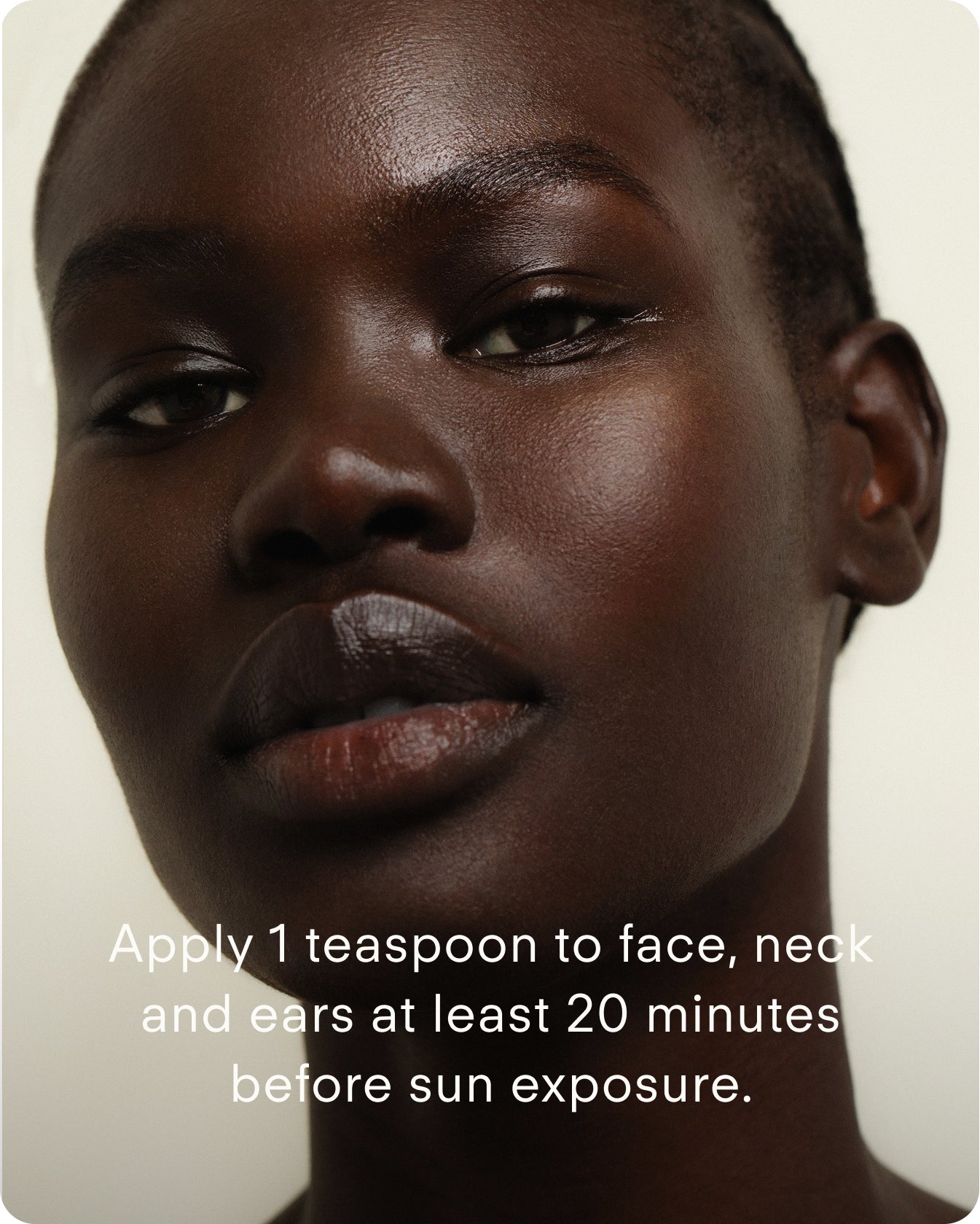 A close-up of a person with smooth, dark skin looking at the camera. Text: Apply 1 tsp of Ultra UV Protective Daily SPF30 Sheer Tint to face, neck, and ears at least 20 minutes before sun exposure.
