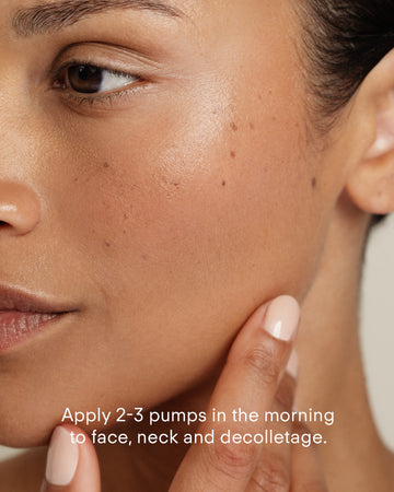 A close-up of a woman applying Ultra B² Hydrating Serum 10mL to her face and neck with her fingers. Text on image: Apply 2-3 pumps each morning to face, neck, and décolletage.