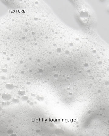 Close-up of Ultra Balancing Gel Cleanser's lightly foaming gel with small and large bubbles on a smooth, white surface, suggesting hydration. The image features the words “TEXTURE” and “Lightly foaming, gel.”.
