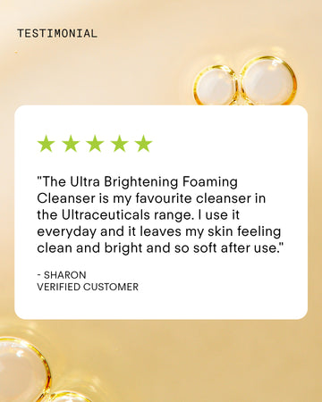 A customer testimonial with five green stars praises the Ultra Brightening Foaming Cleanser, shown on a bubbly light yellow background. The review highlights clean, bright, soft skin—ideal to pair with your Travel Essentials Set.