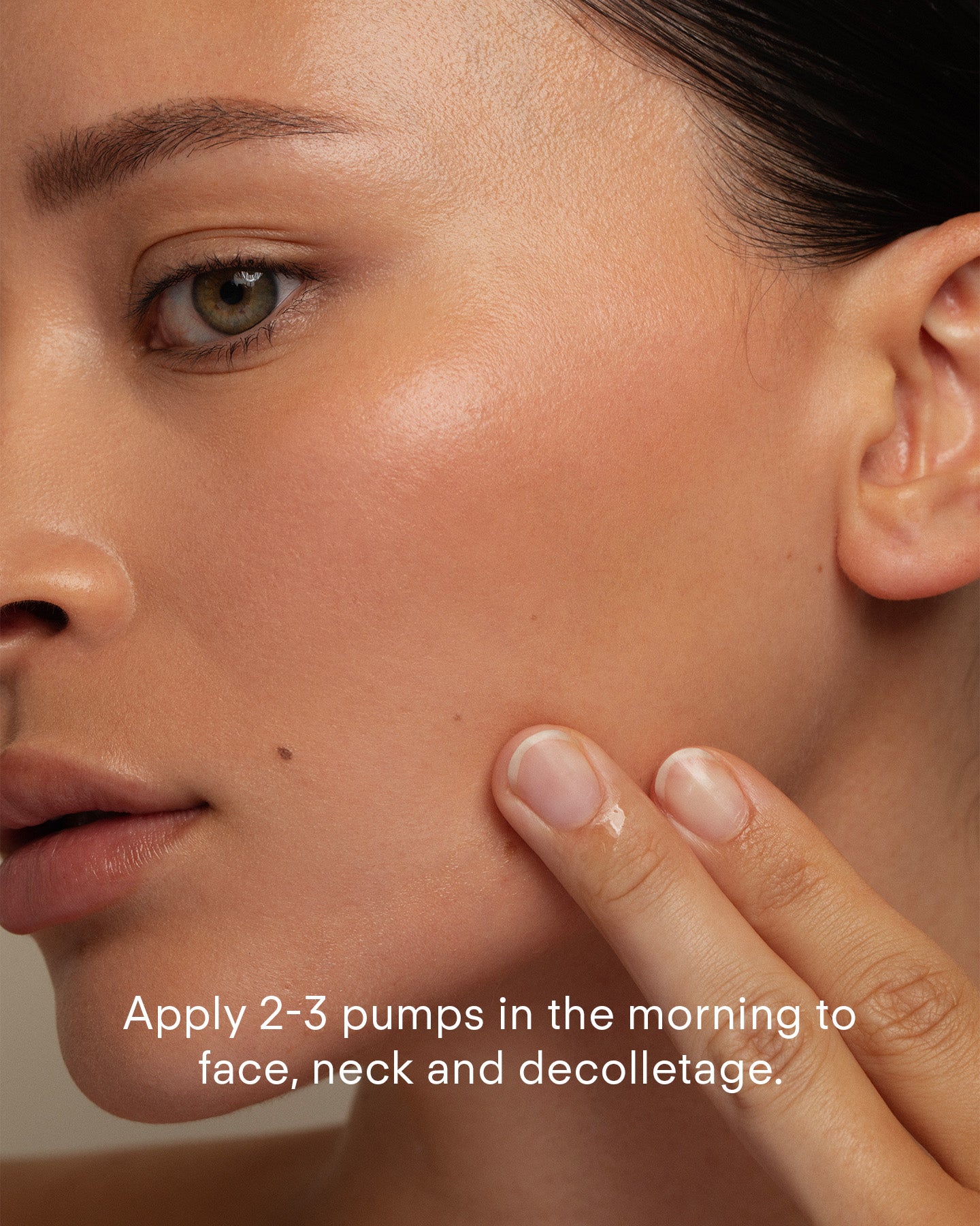 A close-up of a person applying Ultra Brightening Serum Mild to their cheek with their fingers. Text on the image reads: Apply 2-3 pumps to face, neck, and decolletage in the morning.