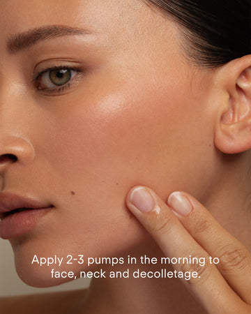 A close-up of a person applying Ultra Brightening Serum Mild to their cheek with their fingers. Text on the image reads: Apply 2-3 pumps to face, neck, and decolletage in the morning.