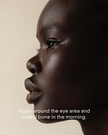 A close-up side profile of a woman with dark skin against a neutral background, with text overlay: Apply Ultra C Firming Eye Cream around the eye area and orbital bone in the morning.